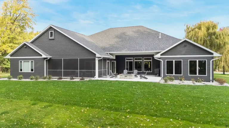 Back view of a custom home with a sunroom and patio with a stone firepit.